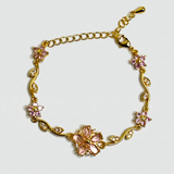 Gold bracelet with pink floral charms on a light gray background
