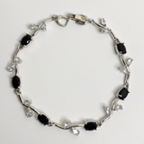 Silver bracelet with black and clear gemstones on a light gray background