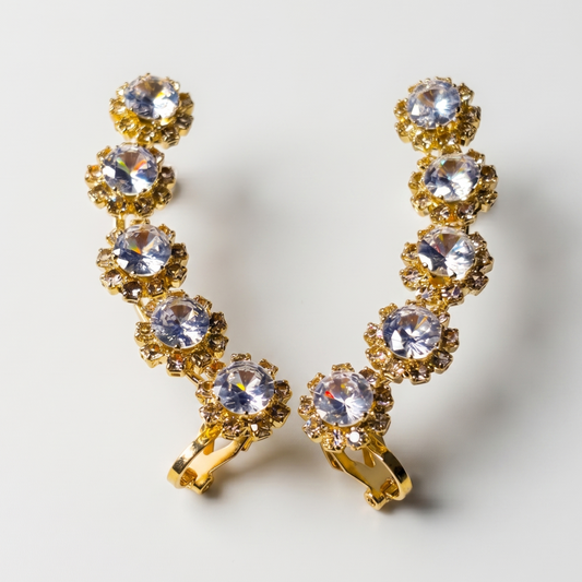 Gold earrings with clear gemstones on a light gray background