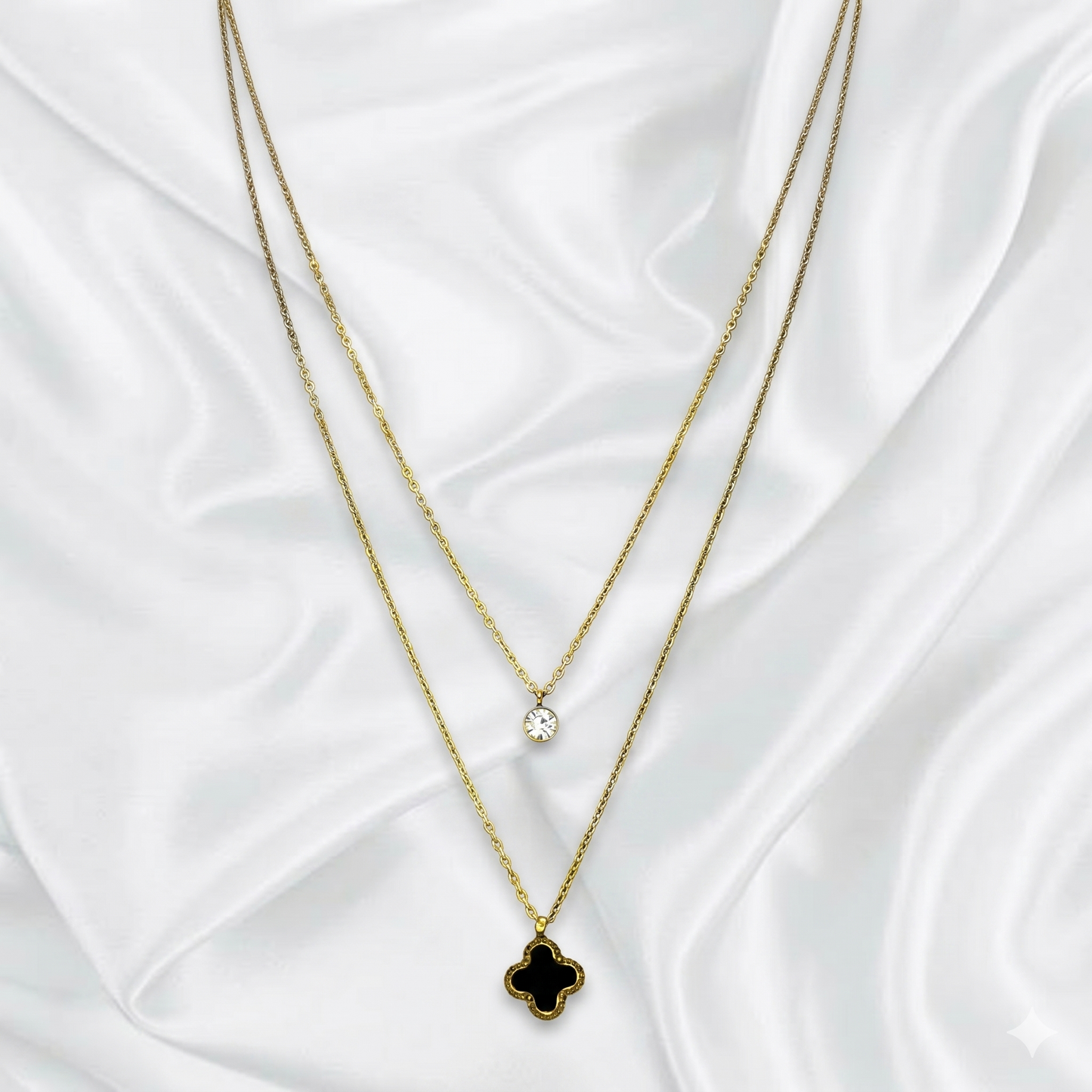 Two layer gold necklaces with clover pendants on a white fabric background