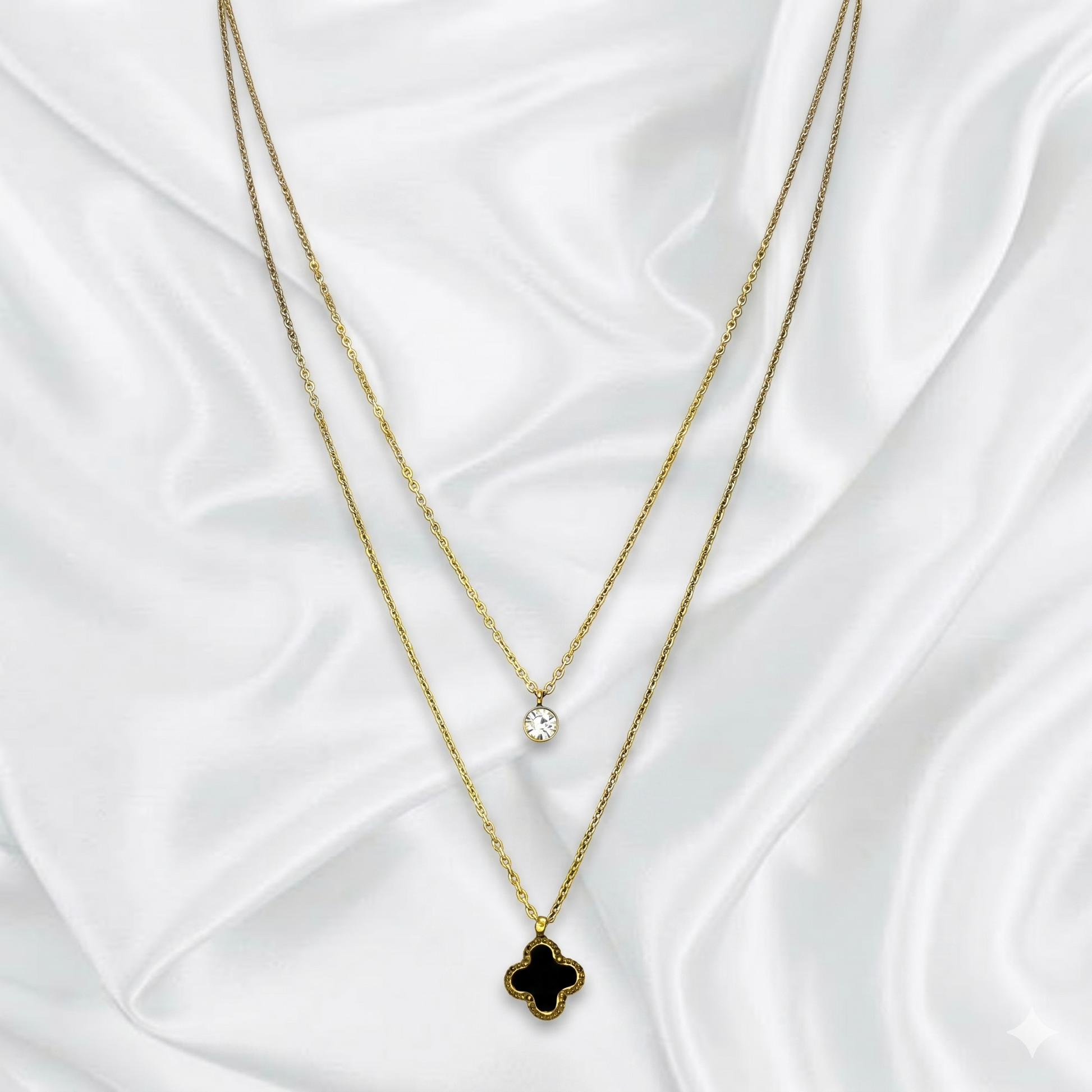 Two layer gold necklaces with clover pendants on a white fabric background