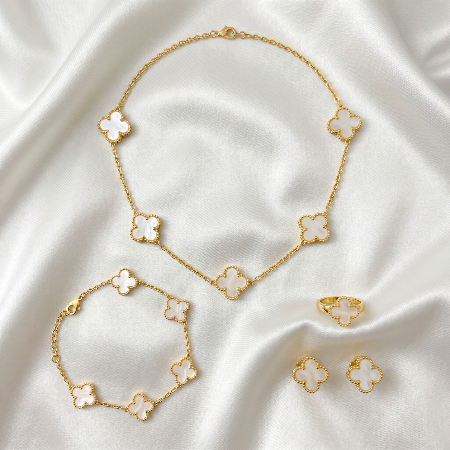 Gold clover necklace, bracelet, ring, and earrings on a white fabric background