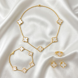 Gold clover necklace, bracelet, ring, and earrings on a white fabric background