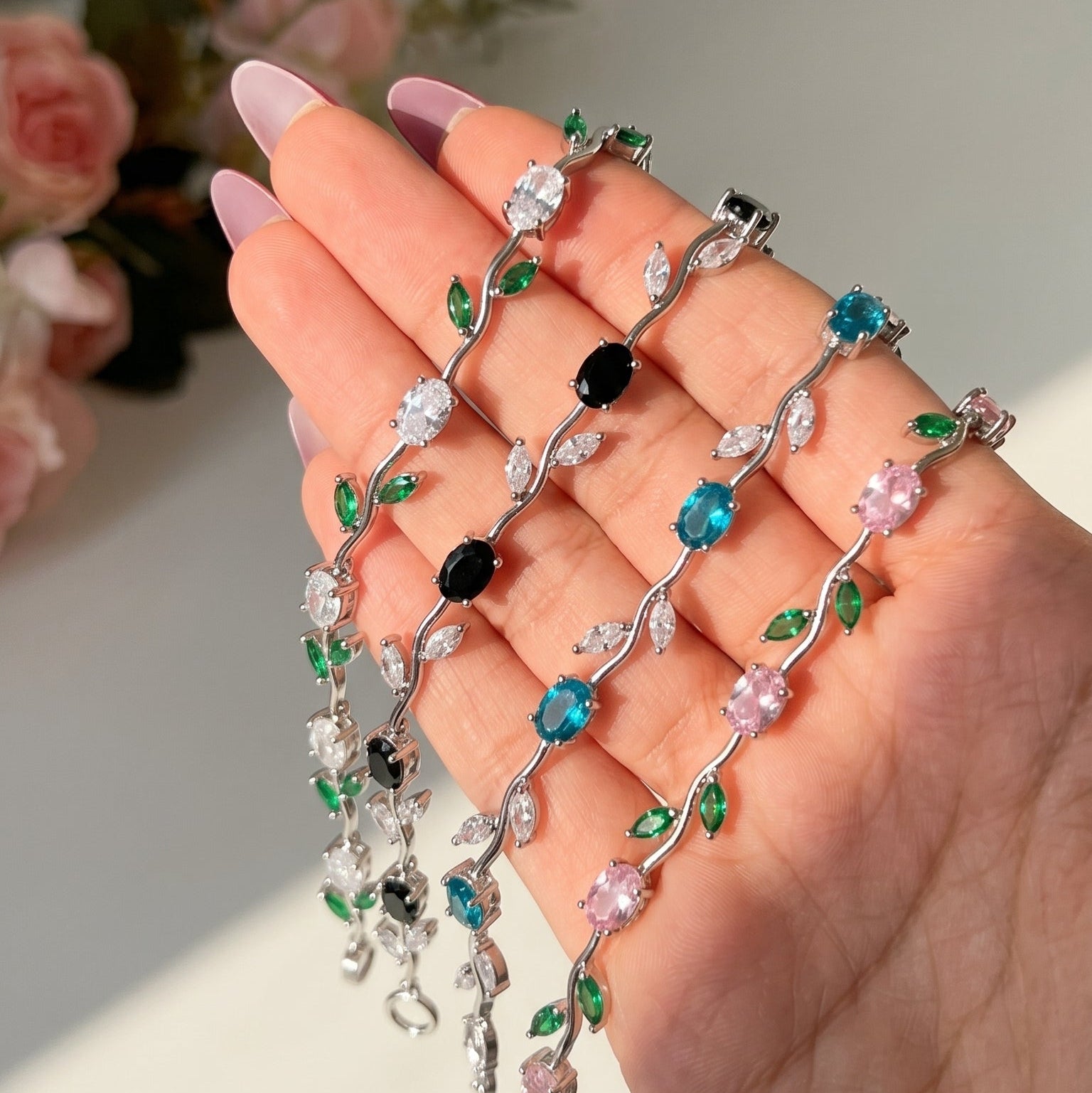 Hand holding 4 decorative necklace with colorful beads against a blurred floral background named bloom vine bracelets