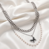 Necklaces with a butterfly pendant and pearl chain on a white fabric background