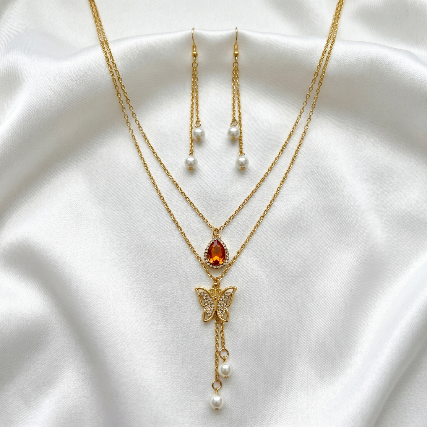 Gold necklace with butterfly pendant and red gemstone on a white fabric background with earrings