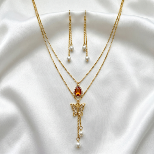 Gold necklace with butterfly pendant and red gemstone on a white fabric background with earrings