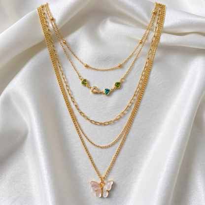 Gold necklaces with butterfly and green gemstone pendants on a white fabric background