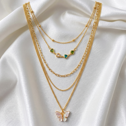 Gold necklaces with butterfly and green gemstone pendants on a white fabric background
