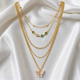 Gold necklaces with butterfly and green gemstone pendants on a white fabric background