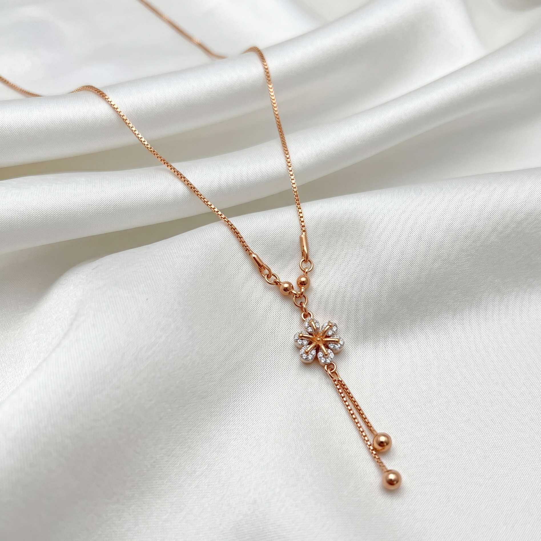 Rose gold necklace with a floral pendant on a white fabric background