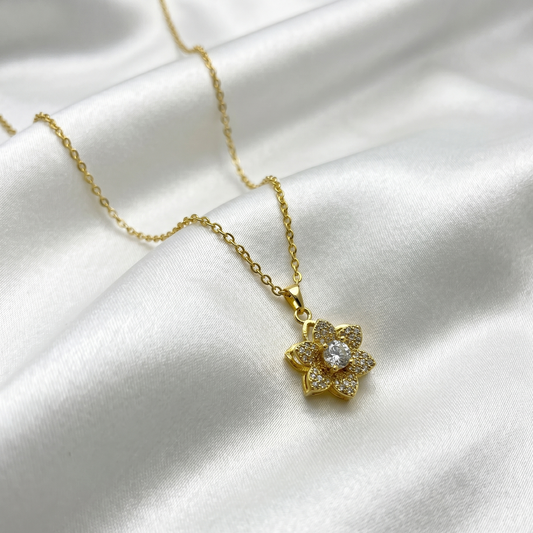 Gold necklace with a floral pendant on a white satin background
