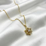 Gold necklace with a floral pendant on a white satin background