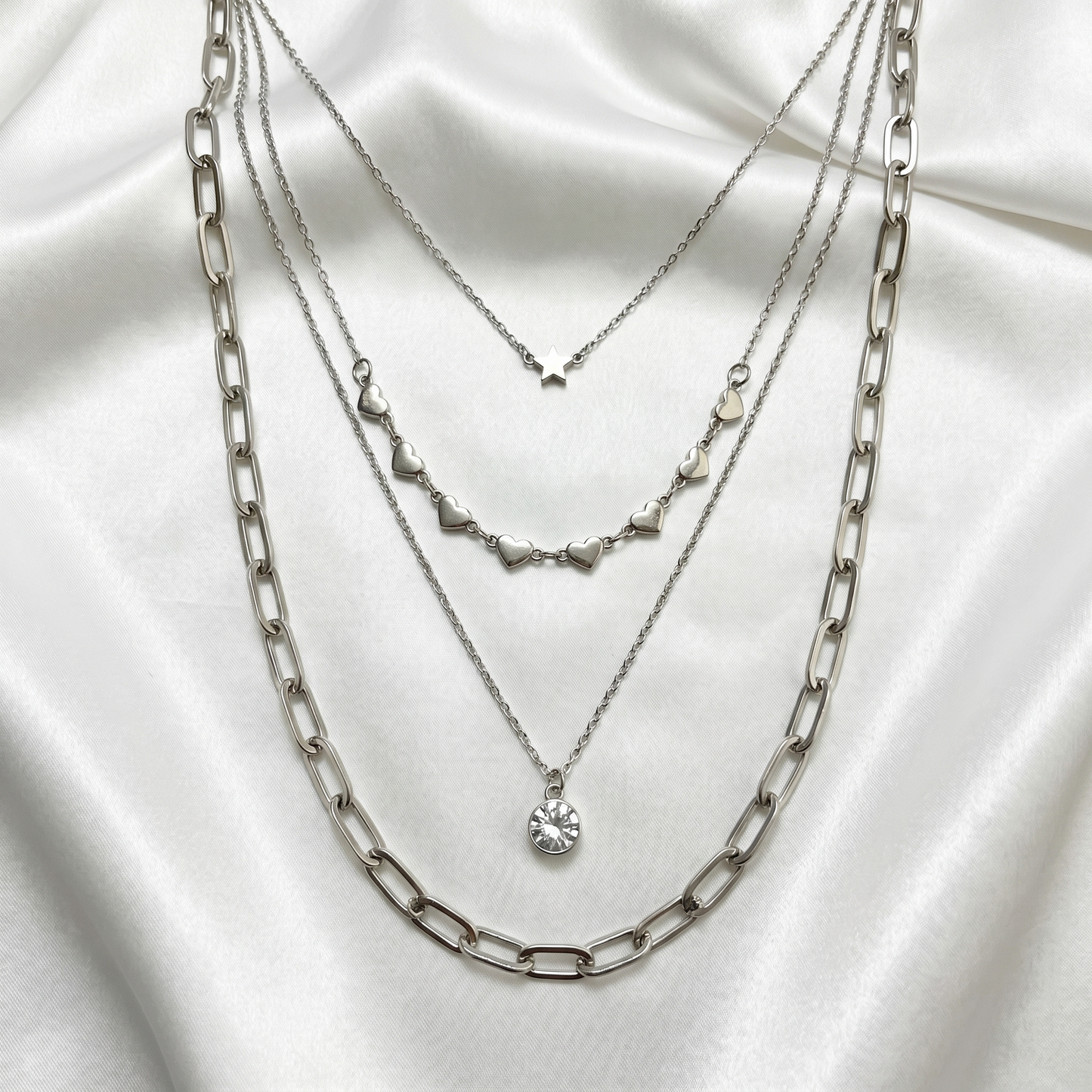 Three silver necklaces layered on a white fabric background