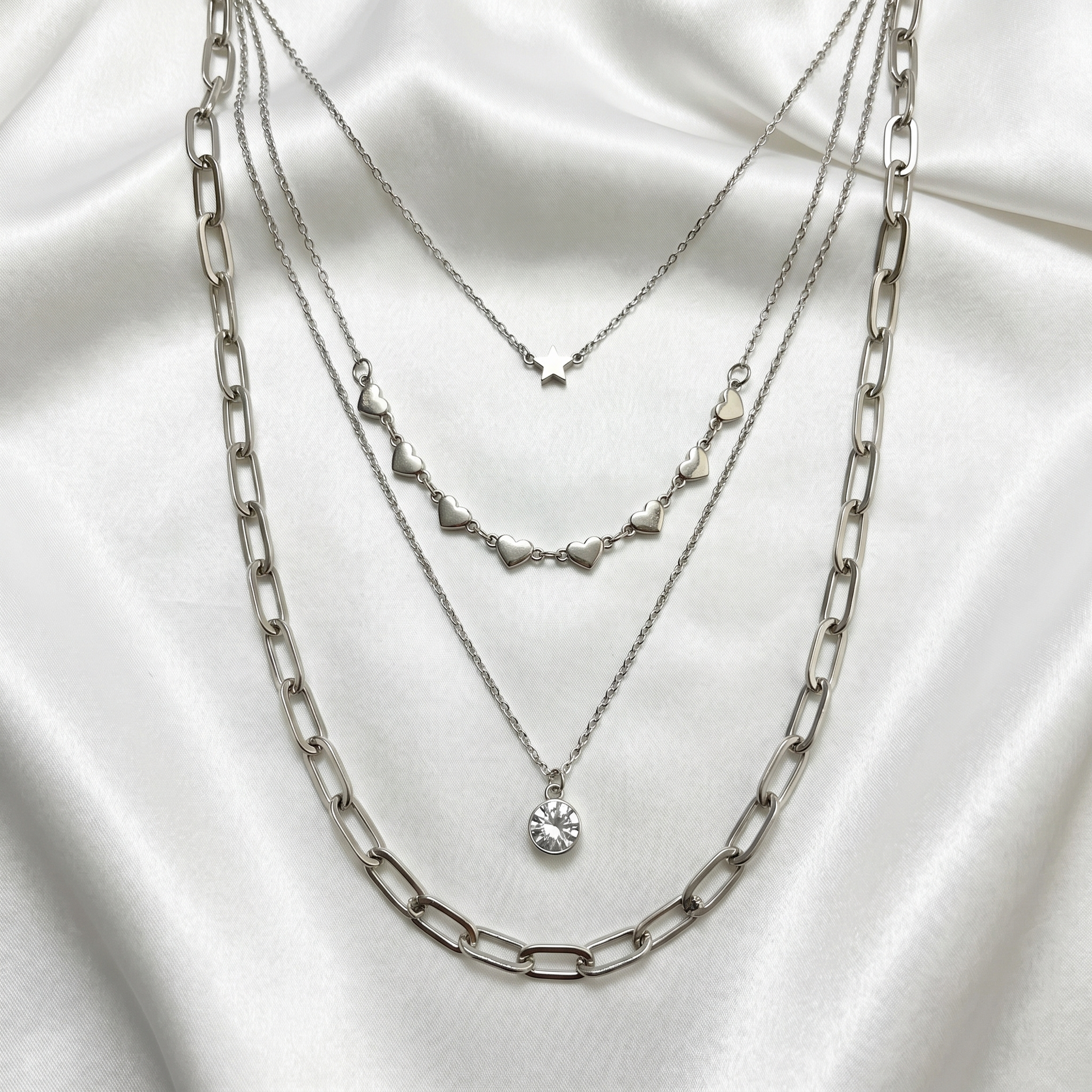 Three silver necklaces layered on a white fabric background