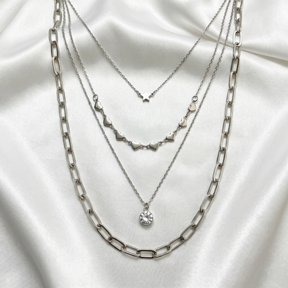 Three silver necklaces layered on a white fabric background