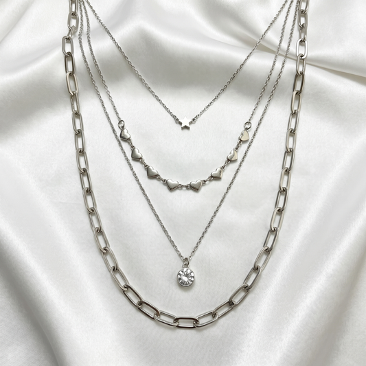 Three silver necklaces layered on a white fabric background