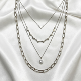 Three silver necklaces layered on a white fabric background