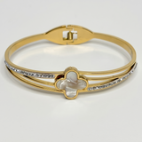 Gold bracelet with a central clover design and diamond accents on a light gray background