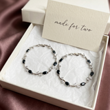 Two silver bracelets with black stones in a box with a 'made for two' card.