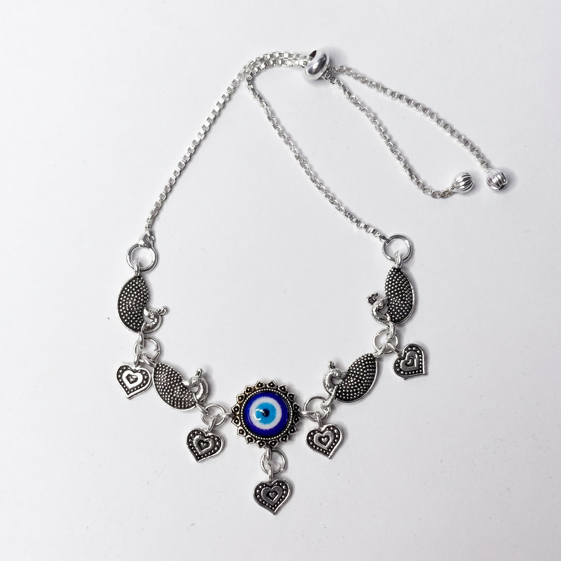 Silver ankletwith heart and eye-shaped charms on a white background