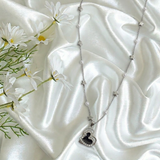 Necklace with a heart-shaped pendant on a white satin surface with flowers.