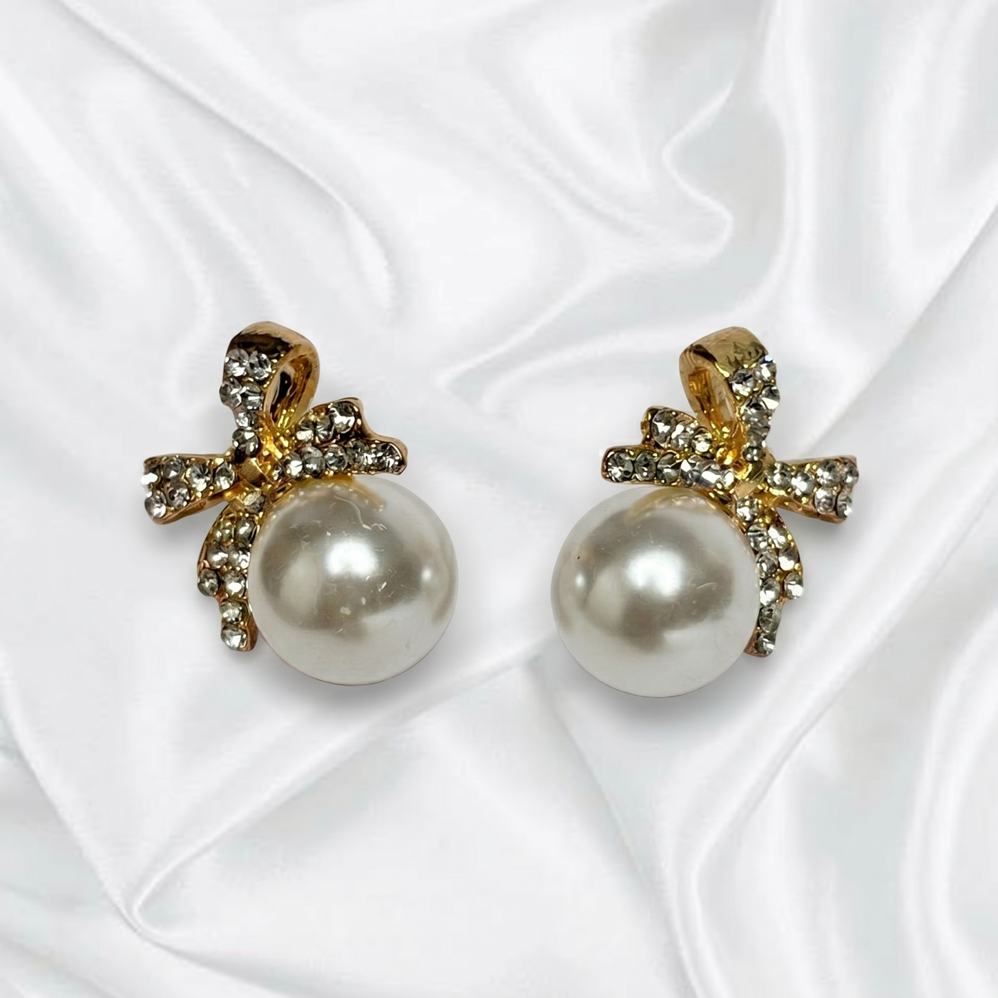 Pearl earrings with gold bows on a white fabric background