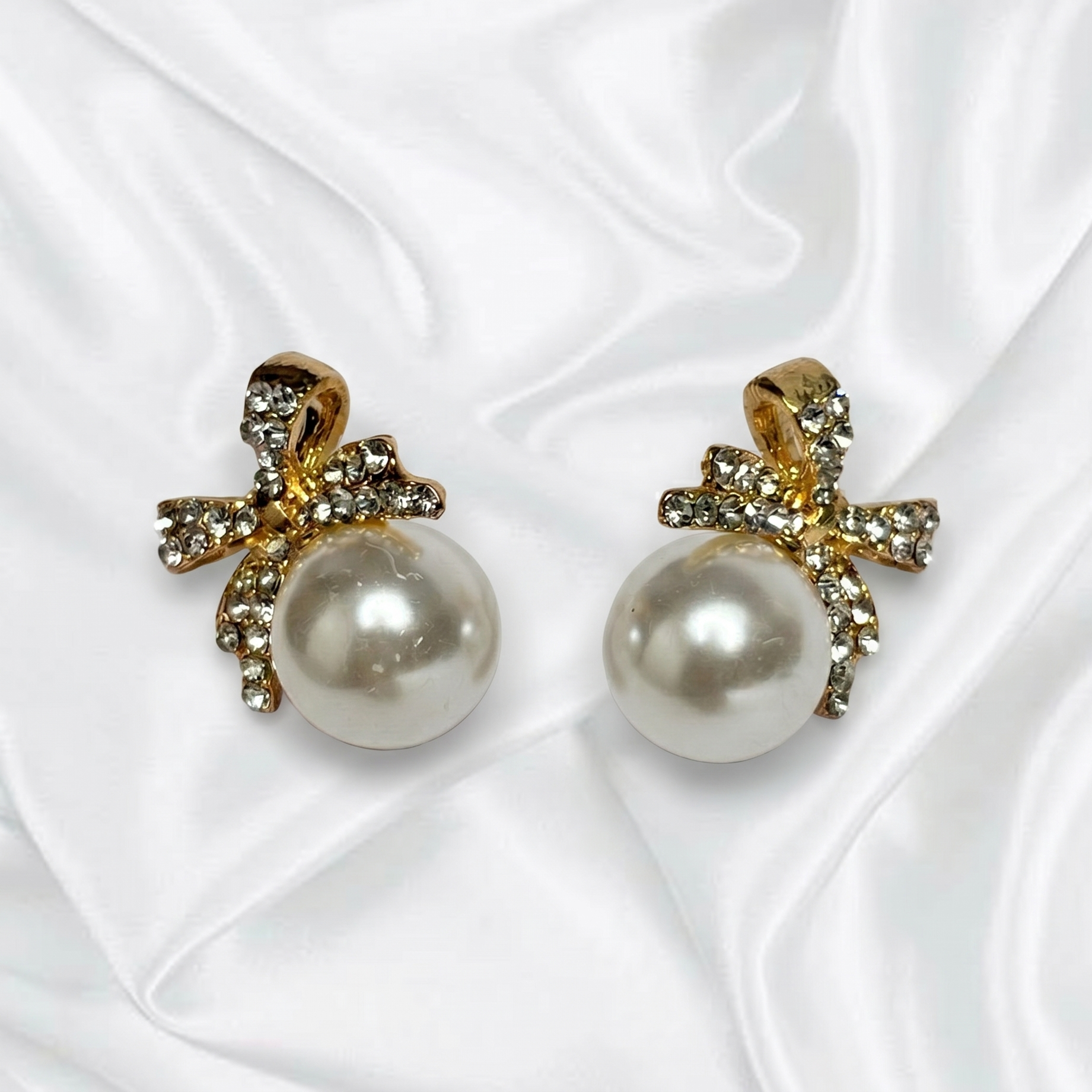 Pearl earrings with gold bows on a white fabric background