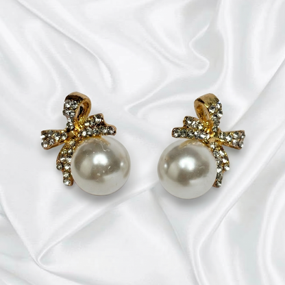 Pearl earrings with gold bows on a white fabric background