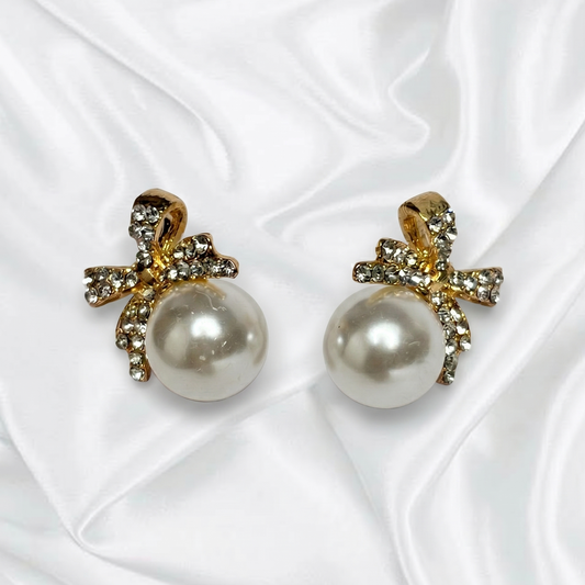Pearl earrings with gold bows on a white fabric background
