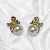 Pearl earrings with gold bows on a white fabric background