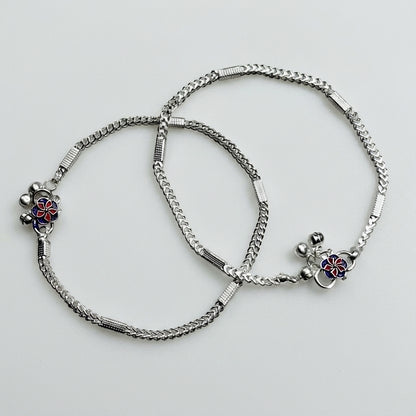 Two silver anklets with floral charms on a light gray background