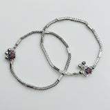 Two silver anklets with floral charms on a light gray background