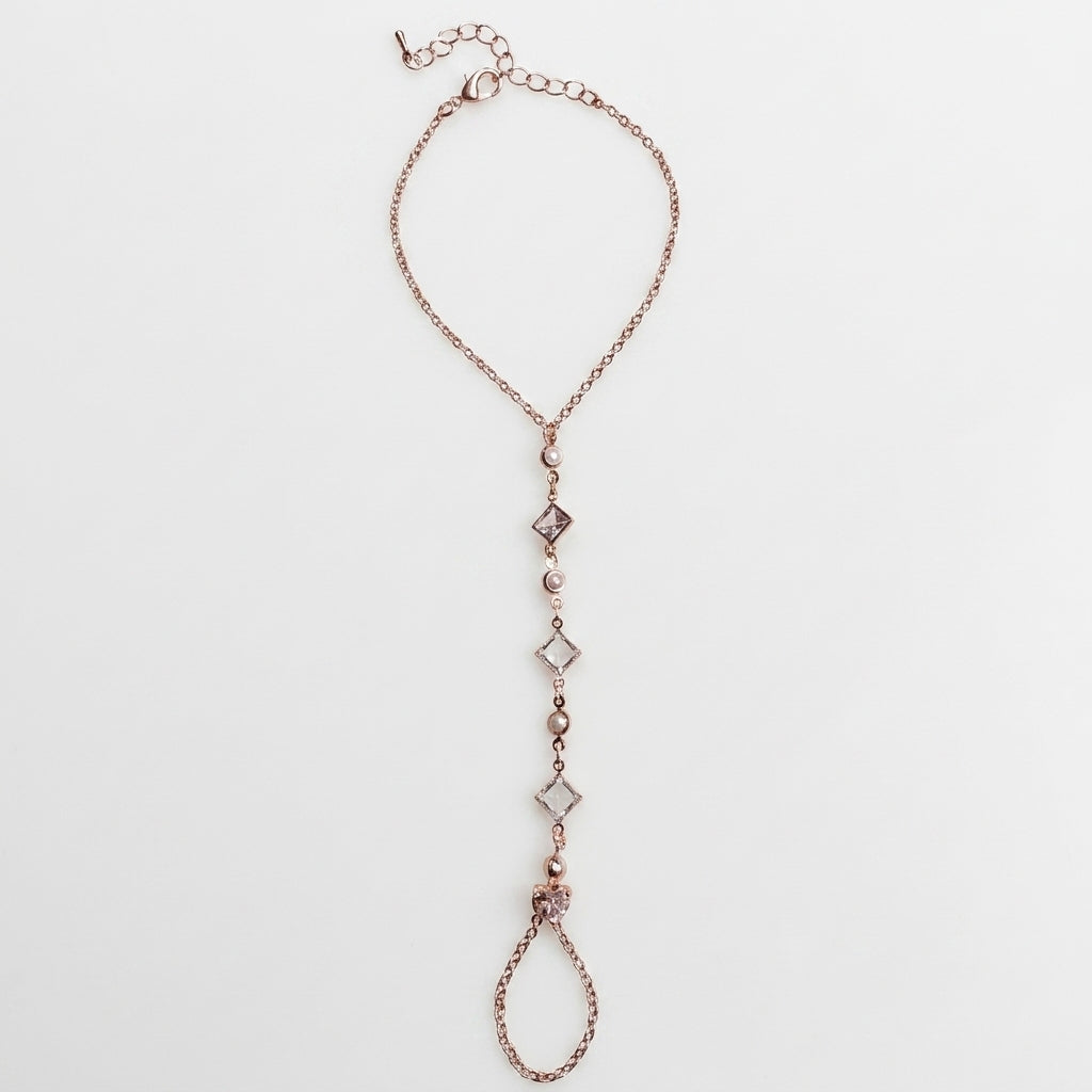 Rose gold hand chain with diamond-like beads on a light gray background