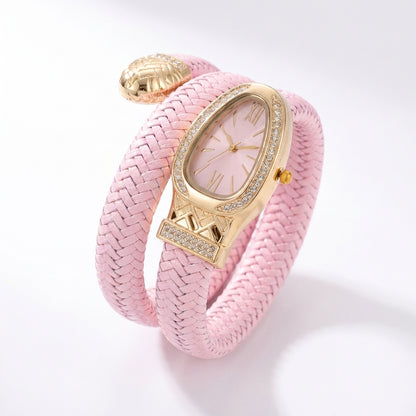 A pink braided wrap bracelet watch with a gold-tone case, crystal-embellished bezel, and a matching pink dial, shown on a clean white background.