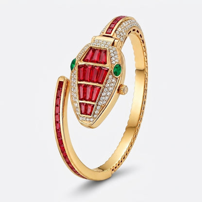 A gold-plated snake-shaped bangle bracelet featuring red baguette-cut stones, small green stones, and clear pavé-set stones, shown on a light gray background.