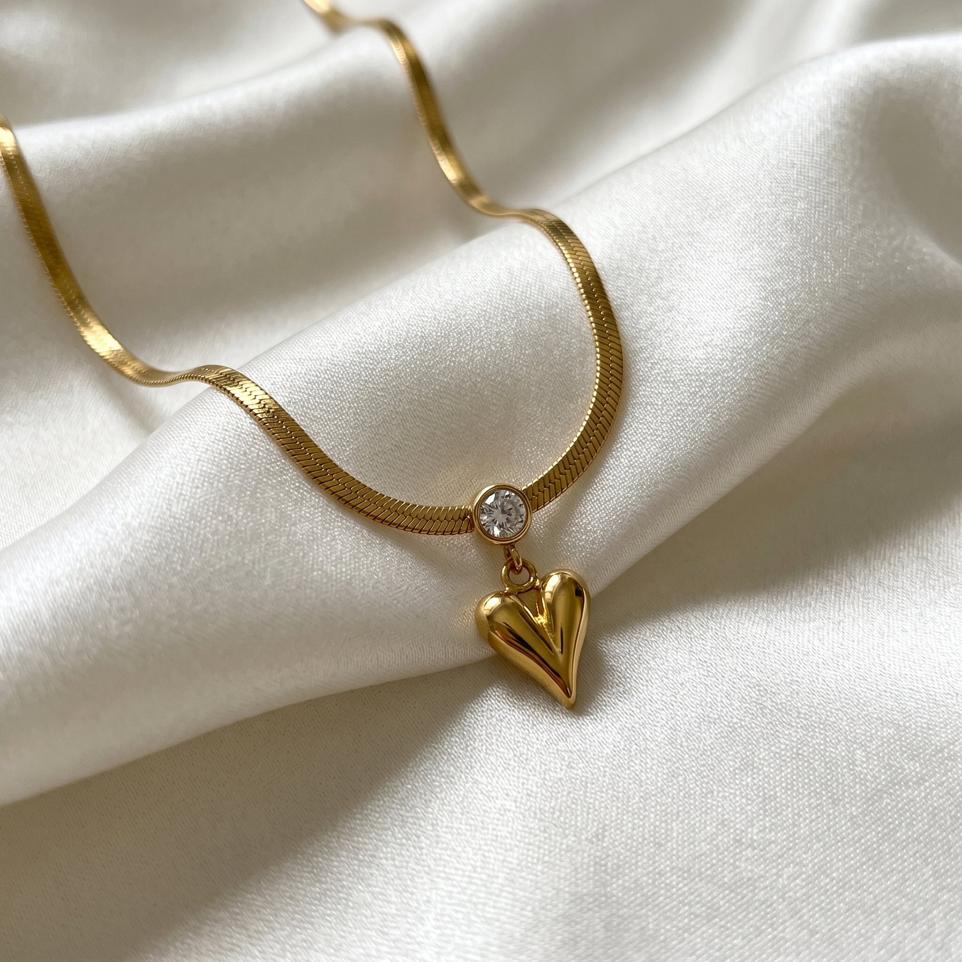 Gold necklace with a heart-shaped pendant on a white fabric background
