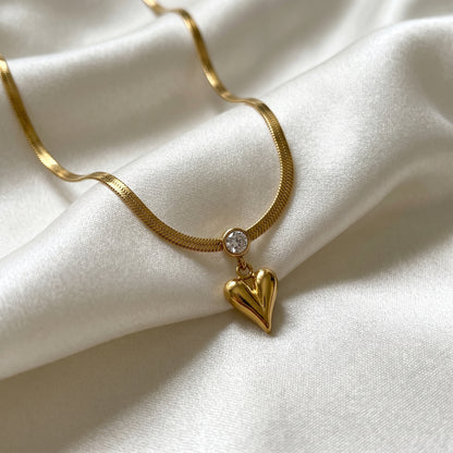 Gold necklace with a heart-shaped pendant on a white fabric background