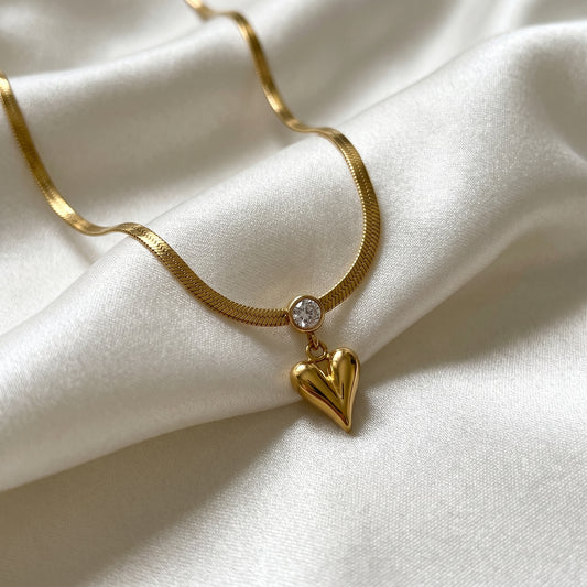 Gold necklace with a heart-shaped pendant on a white fabric background
