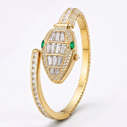 A gold hinged bangle watch featuring a snake-head dial paved with clear baguette and round diamonds, accented by two green emerald-cut gemstones, set against a clean white background.